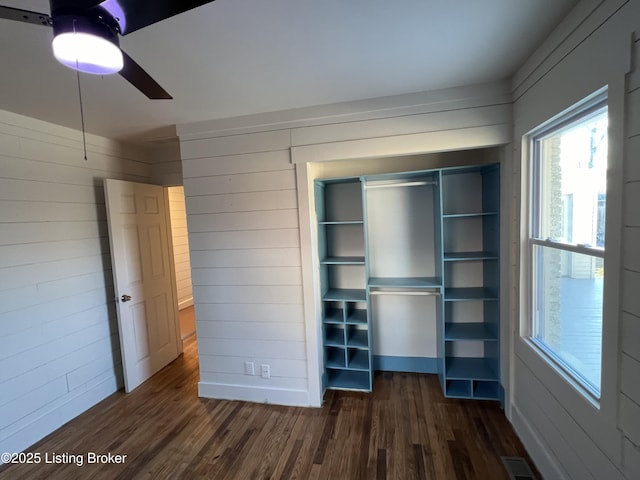 unfurnished bedroom featuring dark wood-style floors, wood walls, a closet, and visible vents