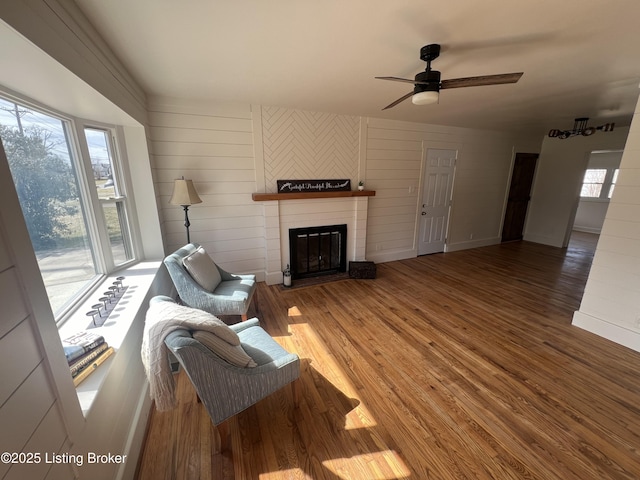 living area with a large fireplace, a ceiling fan, baseboards, and wood finished floors