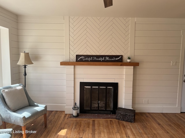 interior space featuring a glass covered fireplace, wood walls, wood finished floors, and baseboards