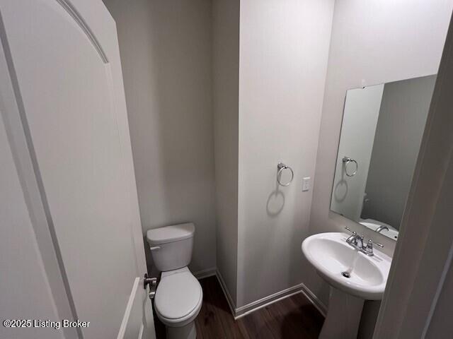 half bath featuring a sink, wood finished floors, toilet, and baseboards