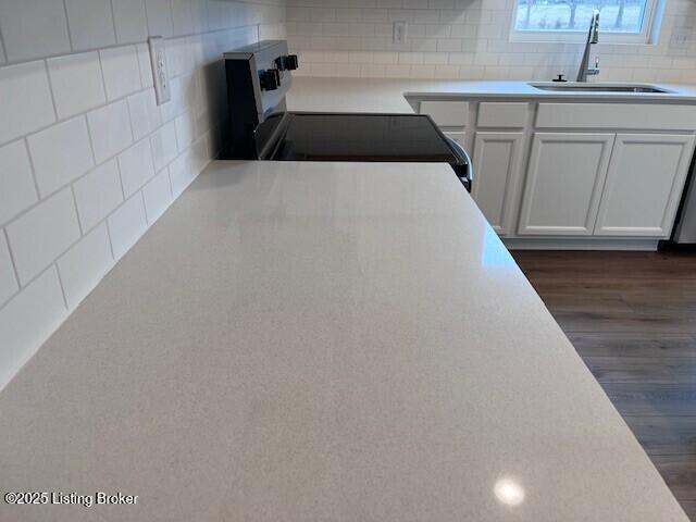 kitchen with electric range, tasteful backsplash, white cabinets, light countertops, and a sink