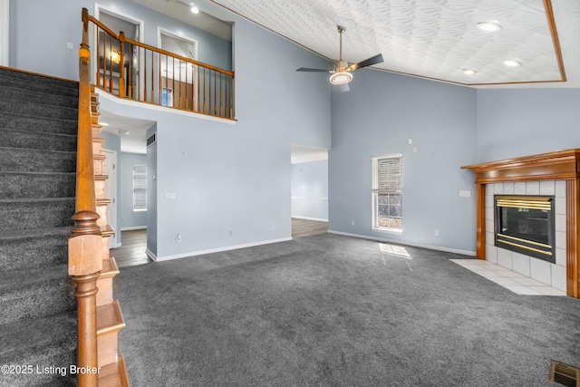 unfurnished living room with carpet, visible vents, ceiling fan, a tile fireplace, and stairs