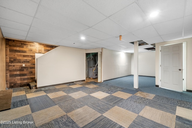 finished basement with wooden walls, baseboards, a drop ceiling, heating unit, and carpet