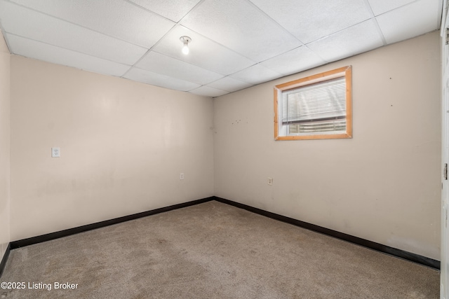 carpeted empty room featuring a paneled ceiling and baseboards