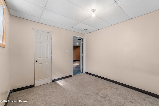 carpeted empty room with visible vents, a paneled ceiling, and baseboards