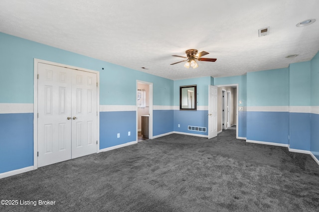 spare room with a ceiling fan, visible vents, dark carpet, and a textured ceiling