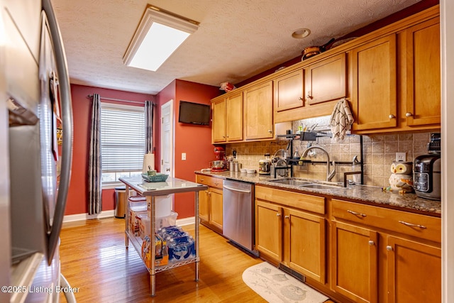 kitchen with light wood finished floors, backsplash, appliances with stainless steel finishes, a sink, and baseboards