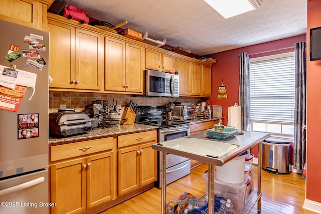 kitchen with appliances with stainless steel finishes, light stone counters, light wood-style flooring, and decorative backsplash