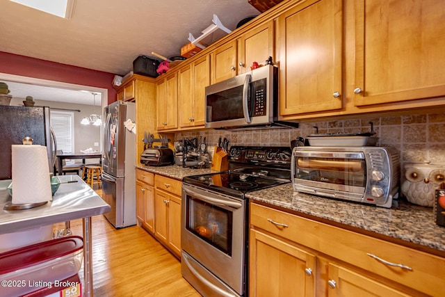 kitchen featuring a toaster, tasteful backsplash, stone countertops, appliances with stainless steel finishes, and light wood-style floors