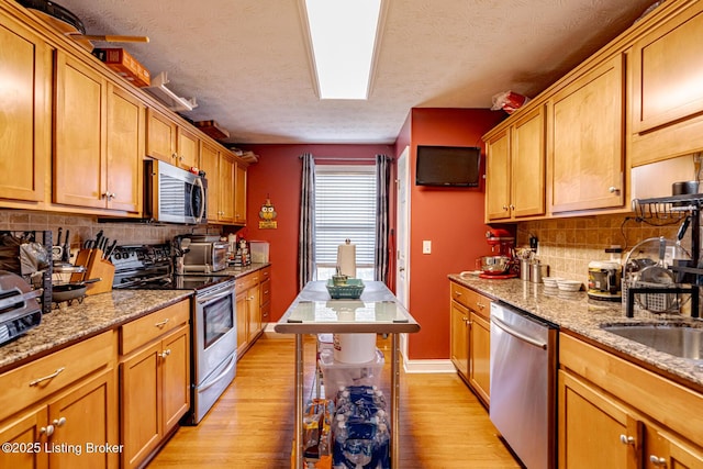 kitchen featuring stainless steel appliances, light stone counters, a sink, and light wood-style flooring