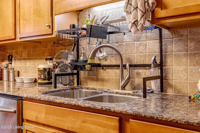 kitchen with tasteful backsplash, stone counters, a sink, and brown cabinetry