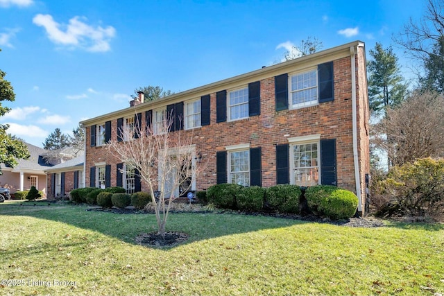 colonial-style house with brick siding, a chimney, and a front yard