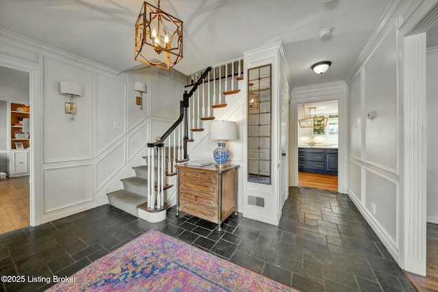 foyer featuring visible vents, stairs, crown molding, stone tile flooring, and a decorative wall