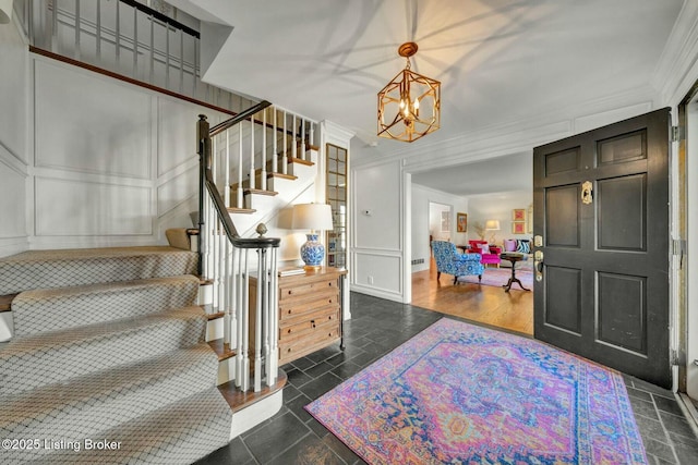 entrance foyer featuring stone tile floors, stairway, ornamental molding, an inviting chandelier, and a decorative wall