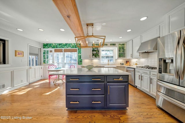 kitchen with stainless steel appliances, wall chimney exhaust hood, light countertops, and white cabinets