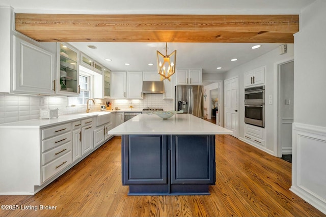 kitchen featuring appliances with stainless steel finishes, white cabinetry, a sink, wood finished floors, and under cabinet range hood