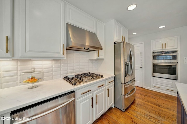 kitchen featuring stainless steel appliances, decorative backsplash, white cabinets, light wood-type flooring, and wall chimney exhaust hood