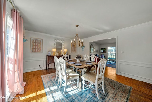 dining space featuring ornamental molding, a decorative wall, wood finished floors, and a notable chandelier