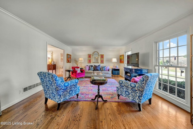 living area with baseboards, wood finished floors, visible vents, and crown molding