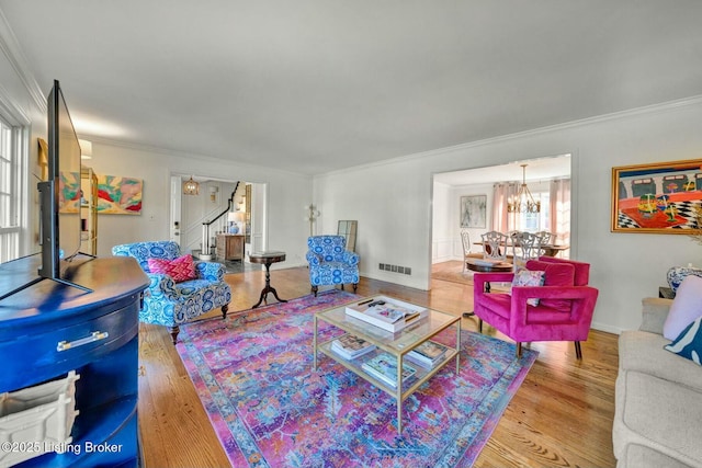 living room with a chandelier, wood finished floors, visible vents, ornamental molding, and stairway