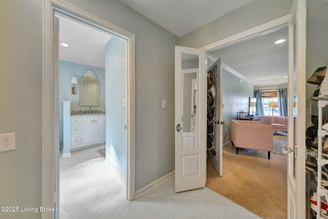 corridor with light carpet, light tile patterned floors, a sink, and baseboards