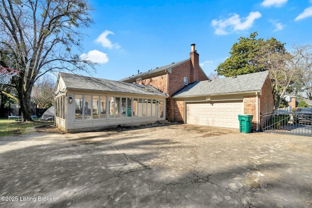 rear view of house with brick siding, a chimney, an attached garage, a sunroom, and driveway