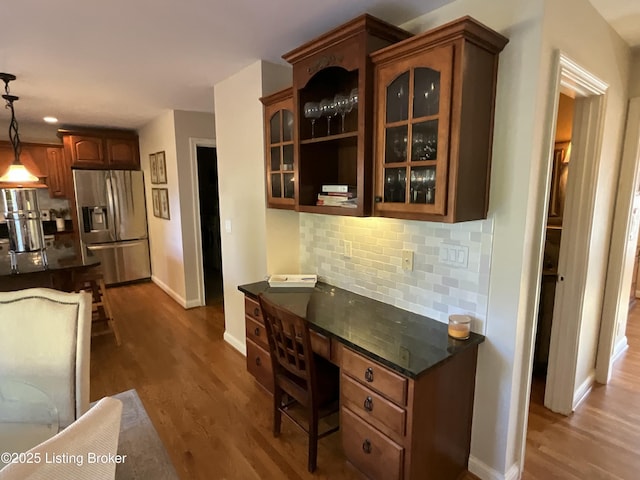 kitchen with dark wood-style flooring, backsplash, built in study area, stainless steel fridge, and glass insert cabinets