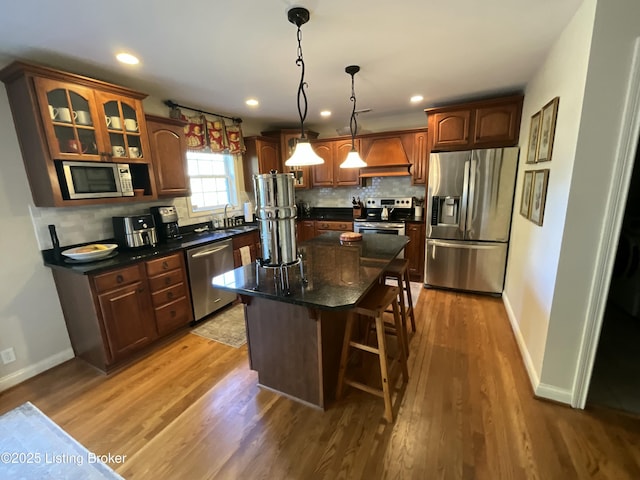 kitchen featuring a breakfast bar, stainless steel appliances, custom range hood, backsplash, and light wood-type flooring