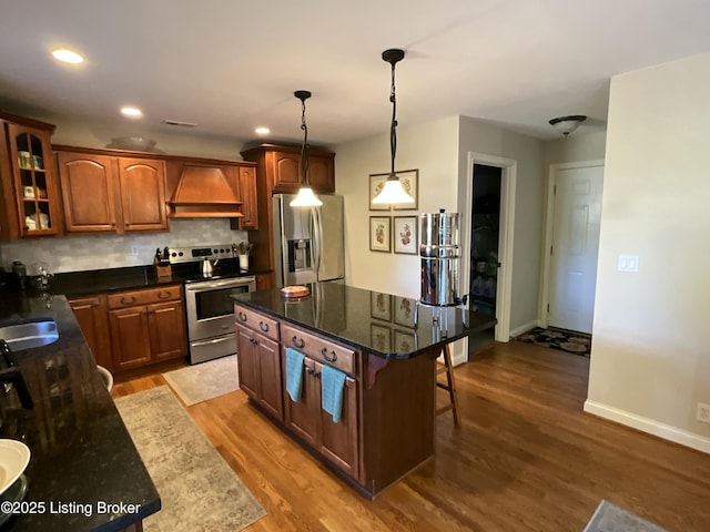 kitchen featuring custom exhaust hood, appliances with stainless steel finishes, a breakfast bar, and wood finished floors