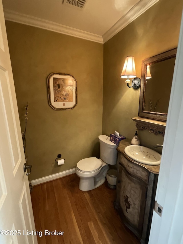 half bathroom featuring toilet, ornamental molding, vanity, wood finished floors, and baseboards