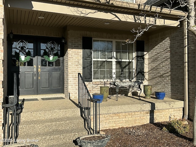 view of exterior entry featuring brick siding, a porch, and french doors