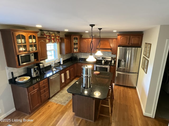 kitchen featuring stainless steel appliances, tasteful backsplash, light wood-style flooring, a sink, and premium range hood