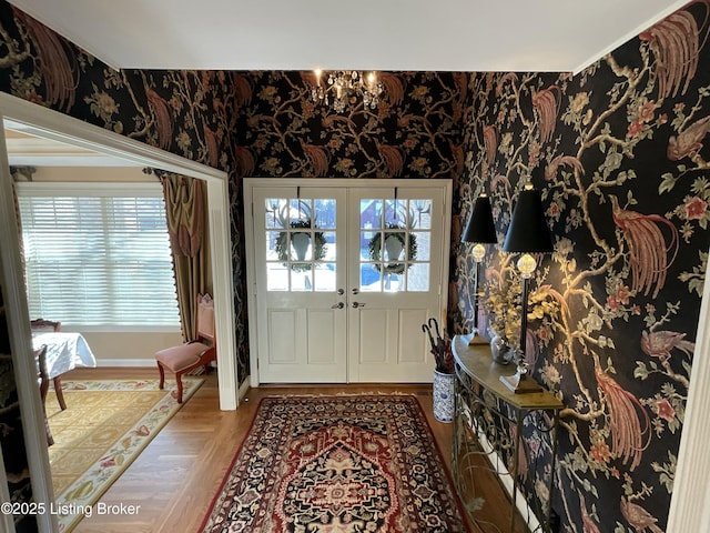 foyer with french doors, a notable chandelier, wood finished floors, baseboards, and wallpapered walls