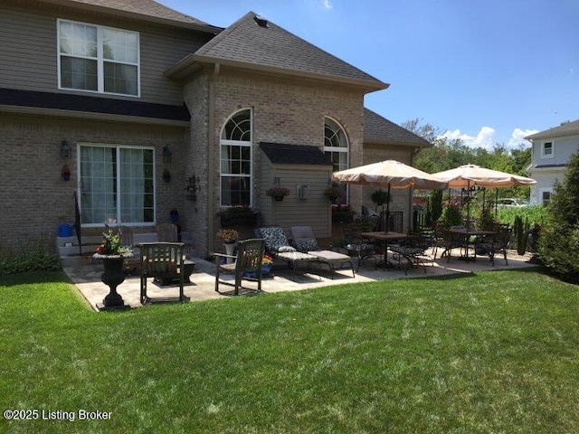 rear view of property with a yard, a patio, brick siding, and a shingled roof