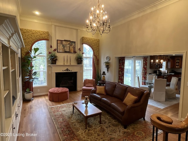 living room featuring baseboards, wood finished floors, crown molding, a fireplace, and a notable chandelier