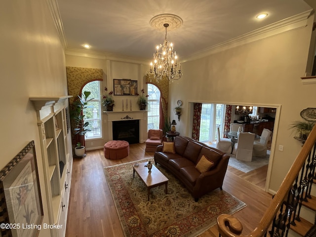 living room featuring ornamental molding, a fireplace, wood finished floors, and a notable chandelier