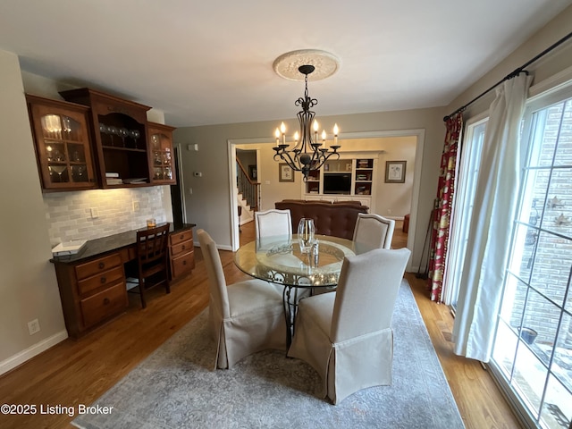 dining space with a notable chandelier, built in desk, stairway, wood finished floors, and baseboards