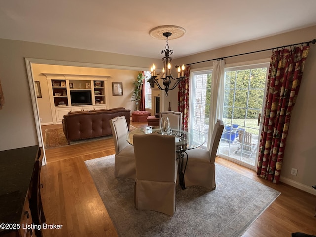 dining area with baseboards, built in shelves, a chandelier, and wood finished floors