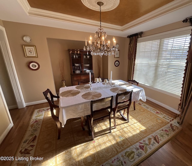 dining room with baseboards, a raised ceiling, crown molding, and wood finished floors