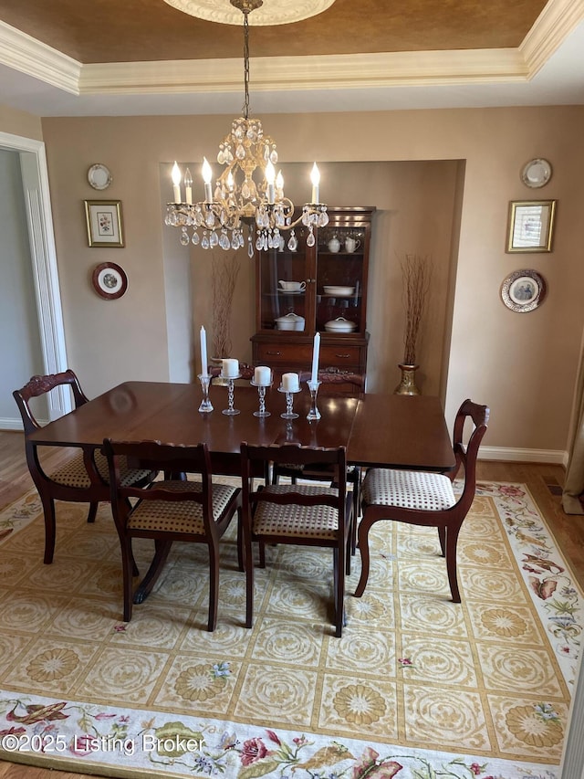 dining area featuring crown molding, a raised ceiling, a notable chandelier, and baseboards