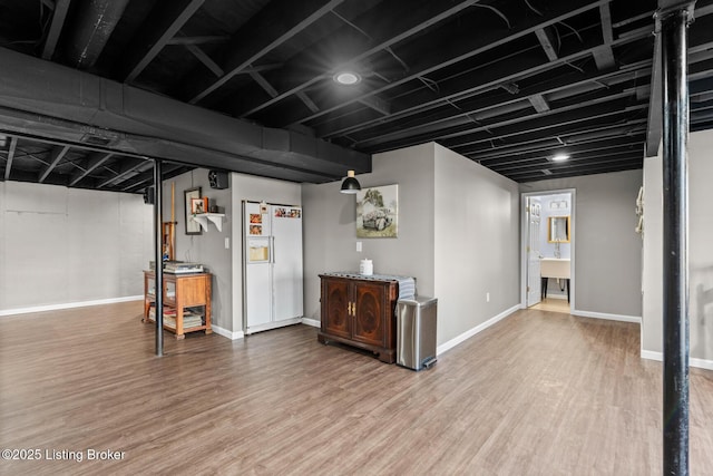 finished basement featuring white refrigerator with ice dispenser, baseboards, and wood finished floors