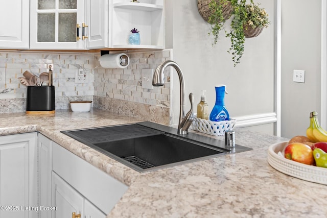 kitchen with tasteful backsplash, glass insert cabinets, light countertops, white cabinetry, and a sink