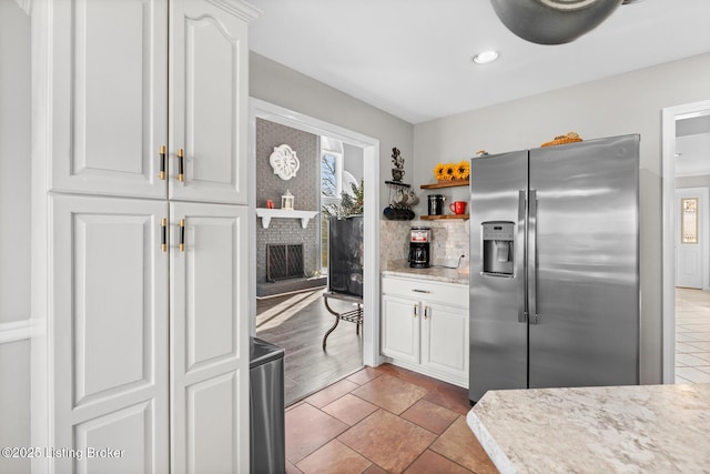 kitchen with a brick fireplace, light countertops, stainless steel refrigerator with ice dispenser, white cabinetry, and open shelves