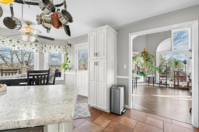 kitchen featuring a wealth of natural light, white cabinets, a ceiling fan, and baseboards