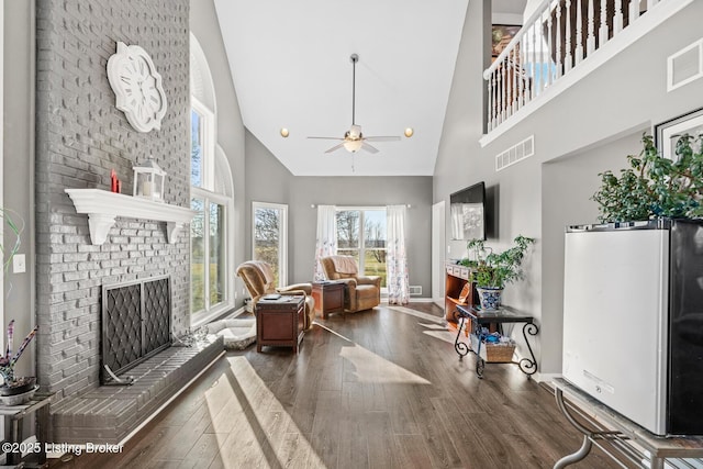 living room featuring wood finished floors, a high ceiling, a fireplace, and visible vents