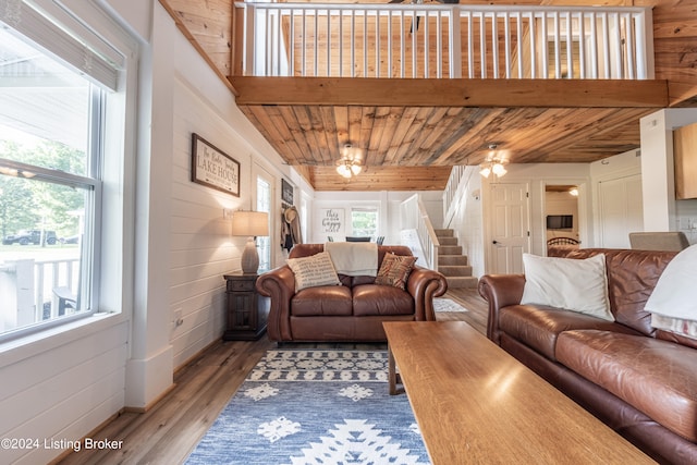 living room featuring wooden ceiling, wood walls, light wood finished floors, and stairs