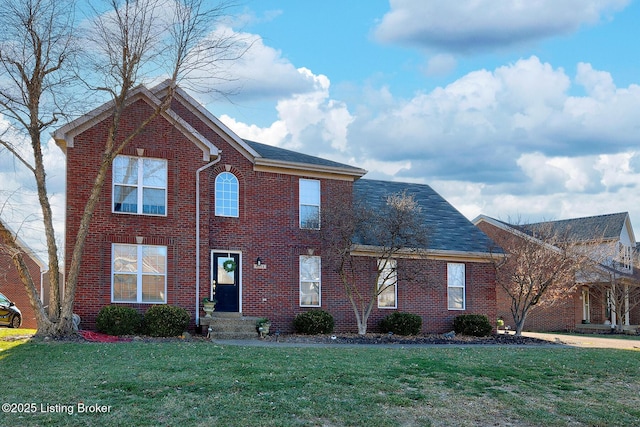 view of front of house with a shingled roof, a front yard, and brick siding