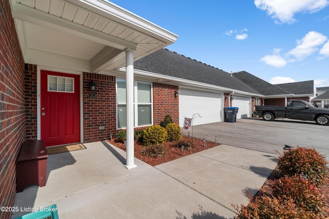 view of exterior entry with a garage, concrete driveway, brick siding, and a shingled roof