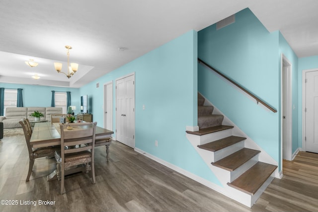 dining area with stairs, a notable chandelier, baseboards, and wood finished floors