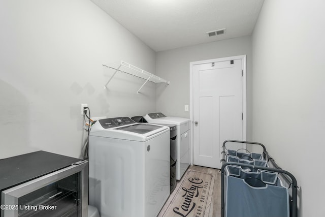 clothes washing area with laundry area, visible vents, light wood-style flooring, a textured ceiling, and washer and dryer